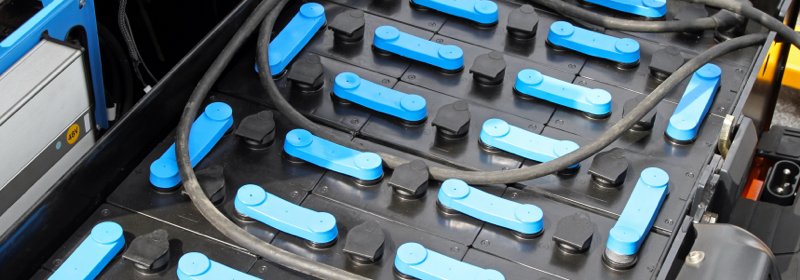 Batterie de chariot élévateur électrique avec câbles de charge et bouchons bleus.