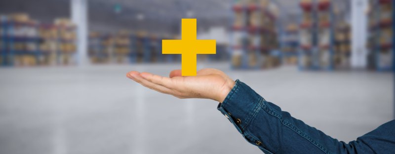 Main tendue sous un symbole plus jaune dans un entrepôt, représentant les avantages de l’achat d’un chariot élévateur pour l’entreprise.