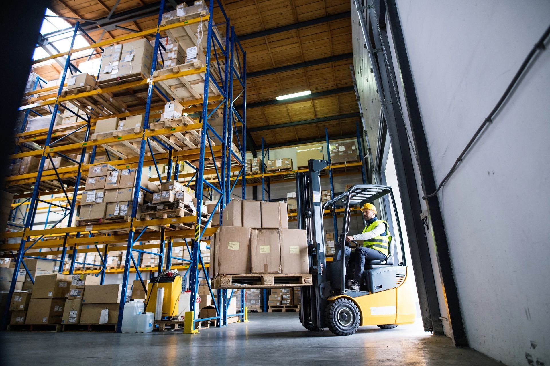 Operator driving a forklift carrying a pallet of boxes in a warehouse, illustrating the safe management of lifting capacity.